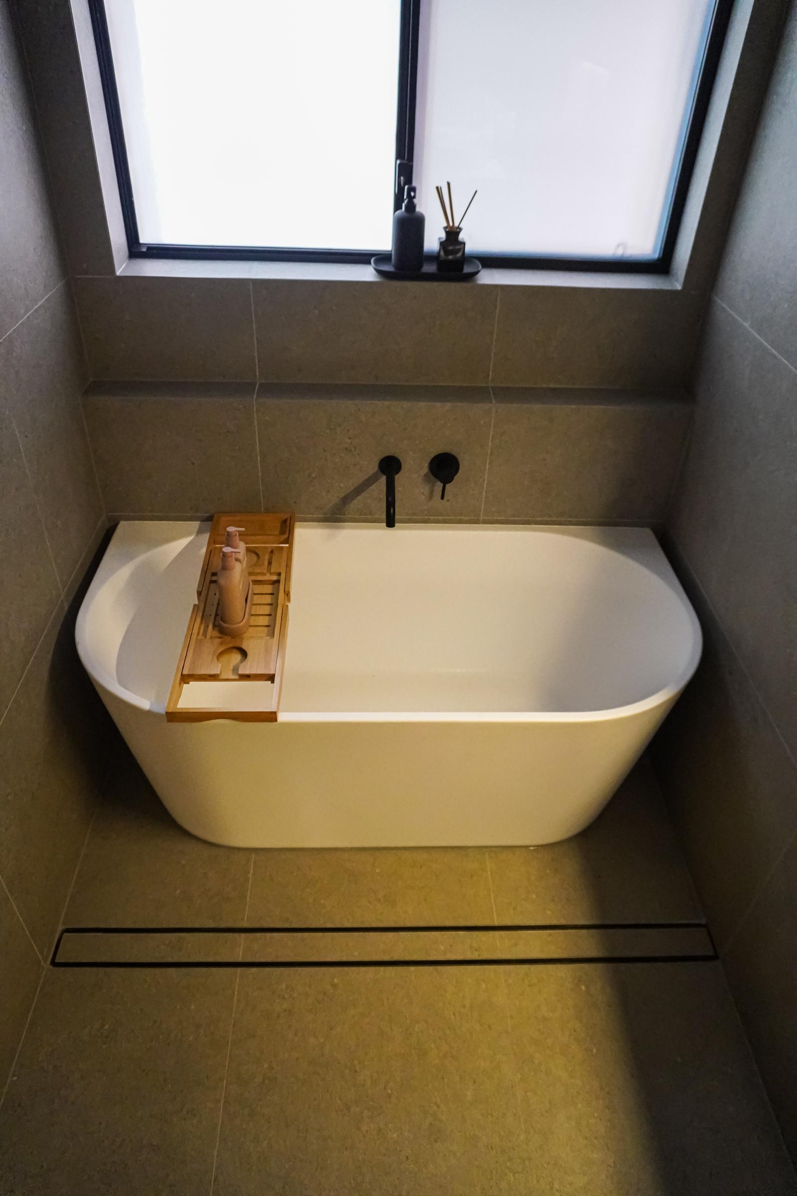 Back-to-wall bath under the window with black wall mixer and linear floor drain, Kingswood bathroom