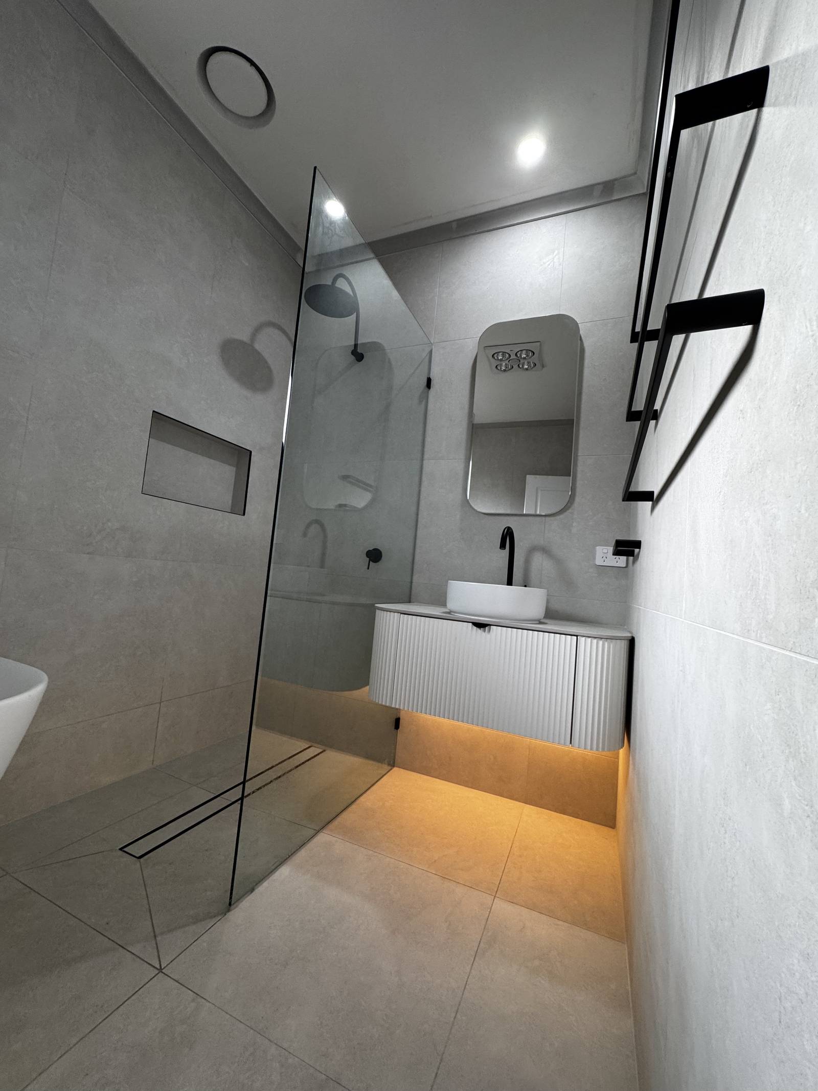 Walk-in shower with a tiled niche, black shower head and linear drain beside a floating fluted vanity, Magill bathroom
