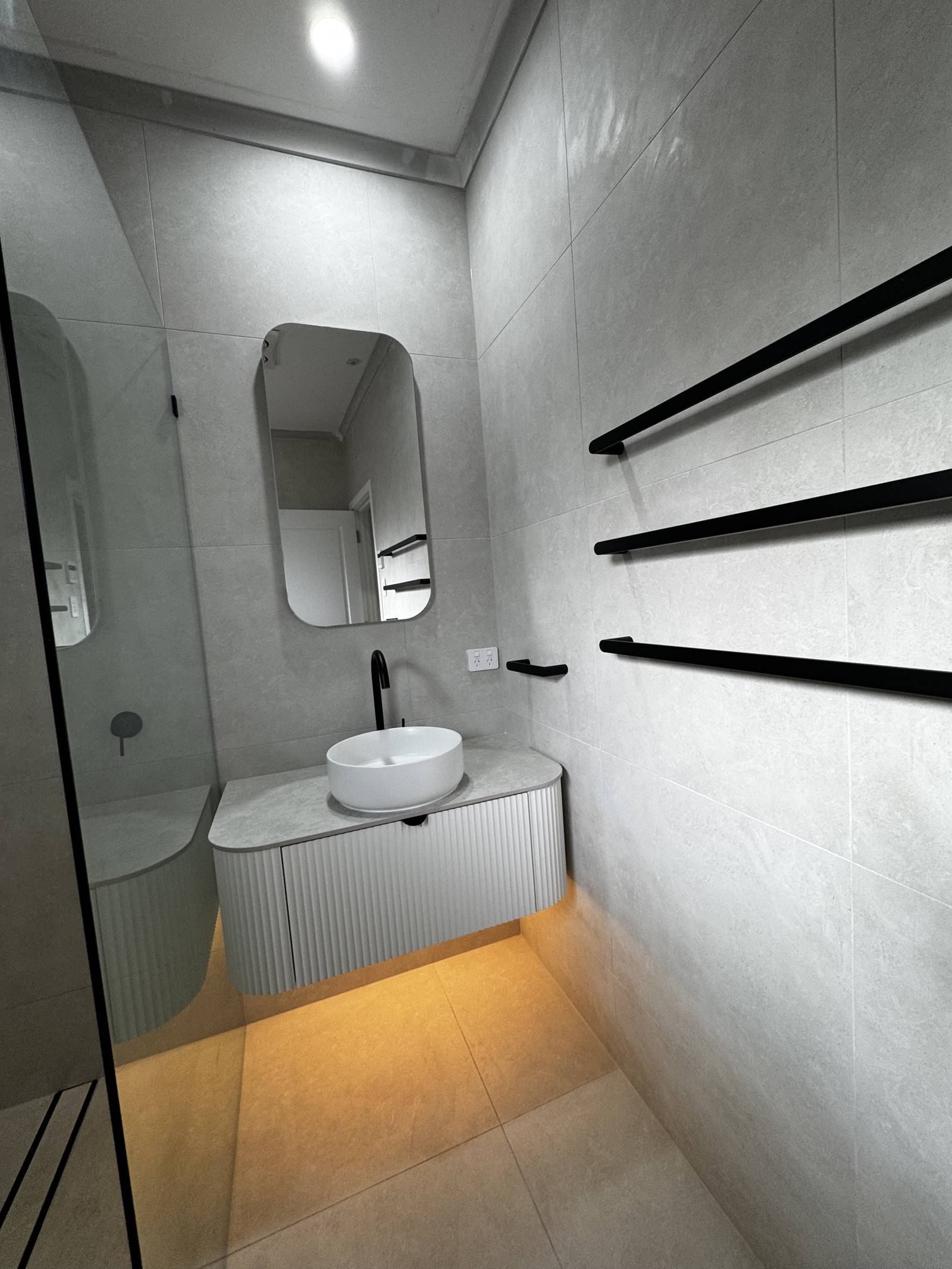 Floating fluted vanity with a vessel basin, LED under-glow, rounded mirror and black towel rails, Magill bathroom