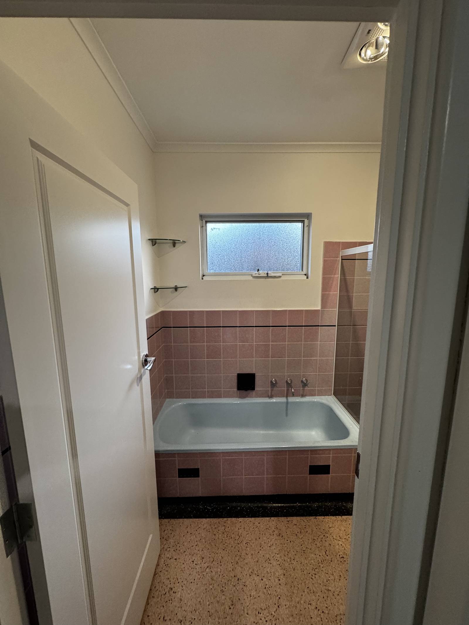 Magill bathroom before the renovation, with pink wall tiles and a pale blue bath under the window