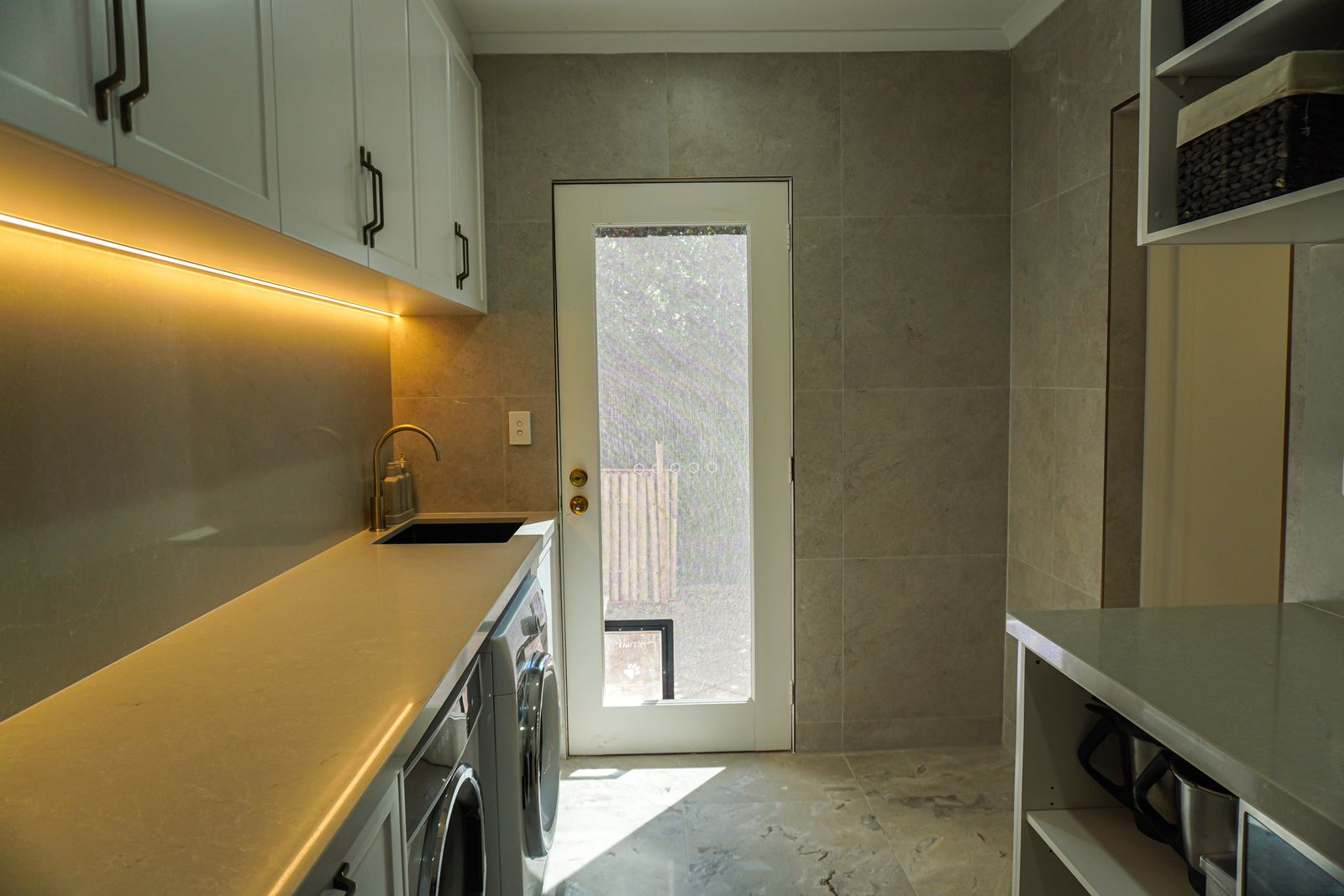 Renovated Torrens Park laundry with LED-lit stone bench over front-loading machines and tiled walls