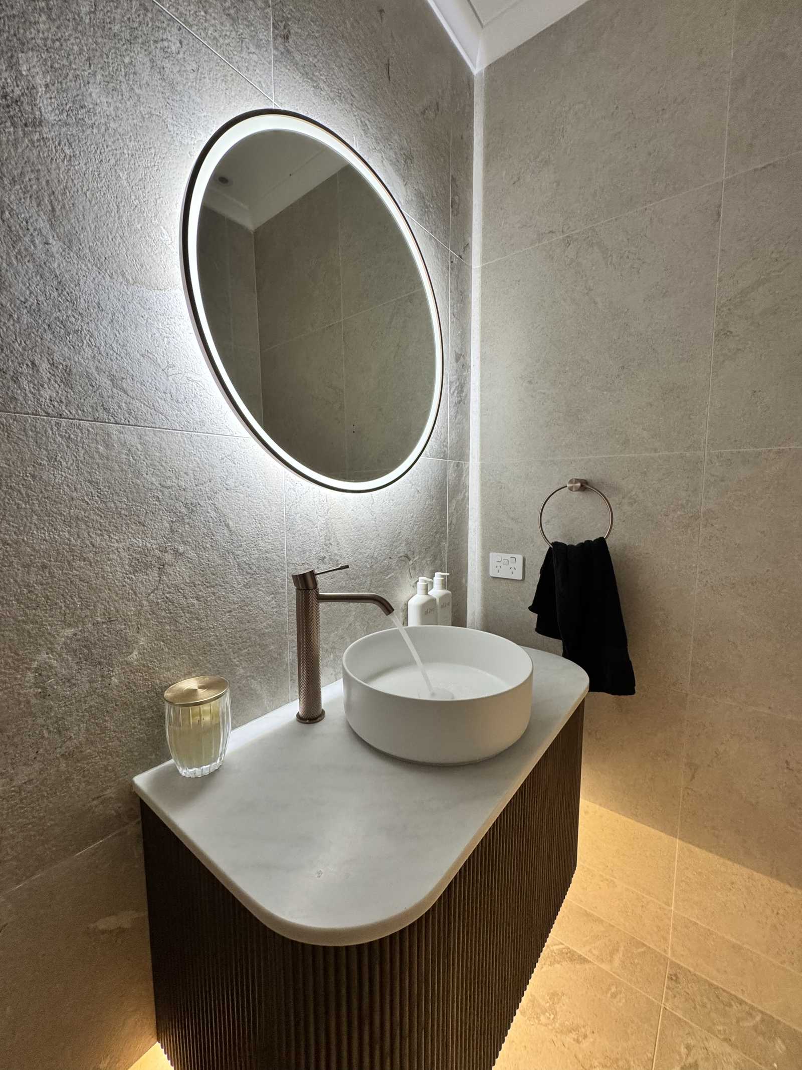 Powder room in Torrens Park at night with backlit round mirror and LED glow under the fluted vanity
